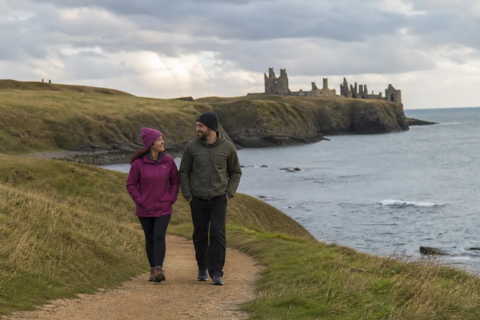 A couple walking beside Bamburgh beach with the castle in the distance